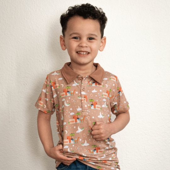 A child wearing a beige polo shirt with a printed design featuring desert scenes and cultural motifs.