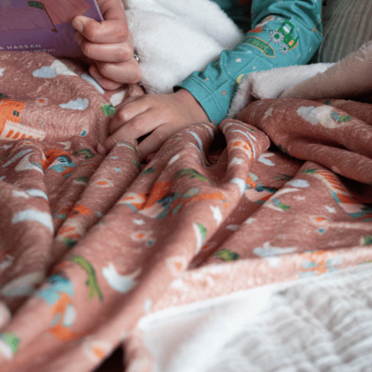 Child reading a book on a bed with a pink blanket