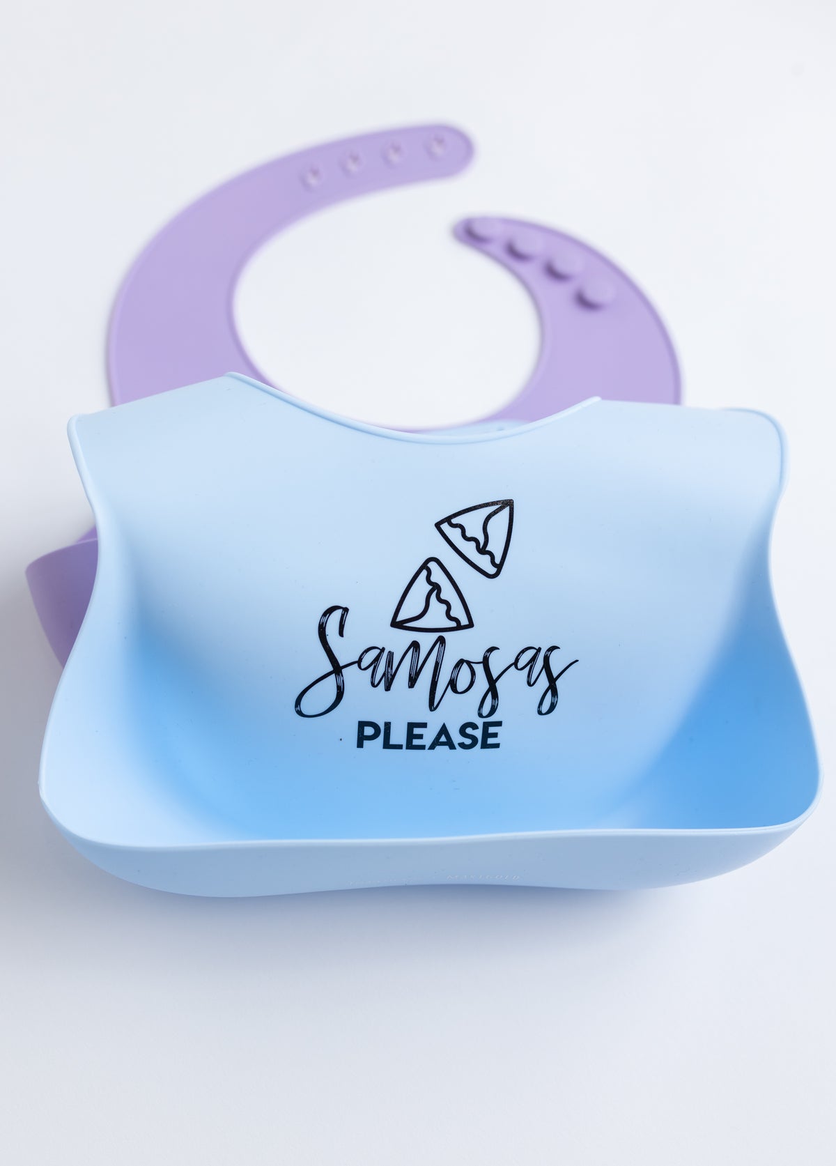 Blue Samosas Please bib laying on top of a purple bib.