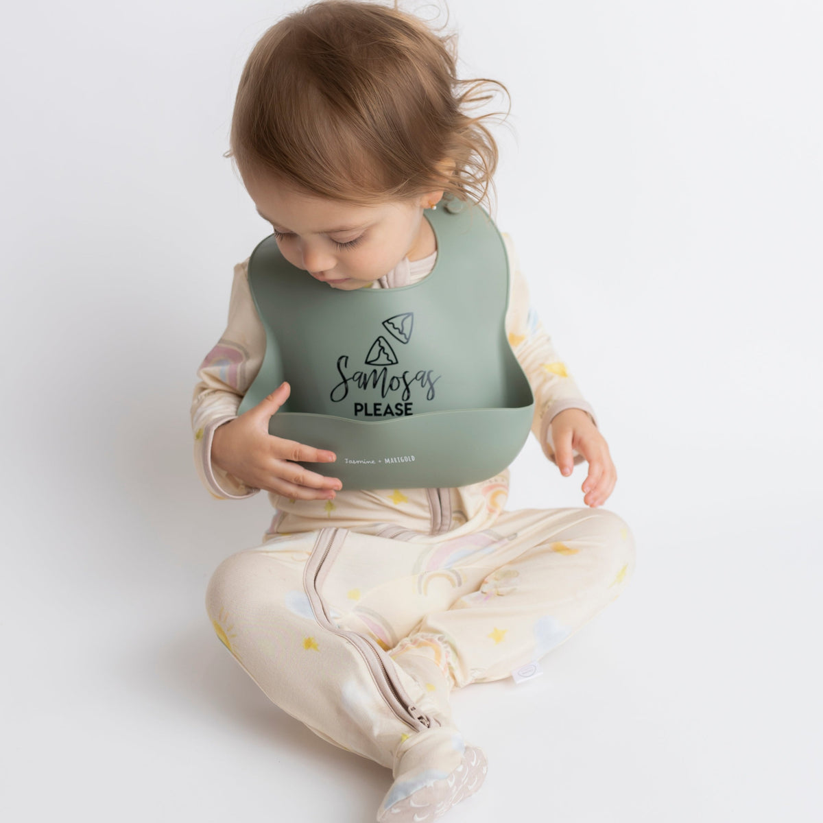 18 month old infant wearing oversized green (olive) colored Samosas Please bib.  Baby is looking down at her bib.