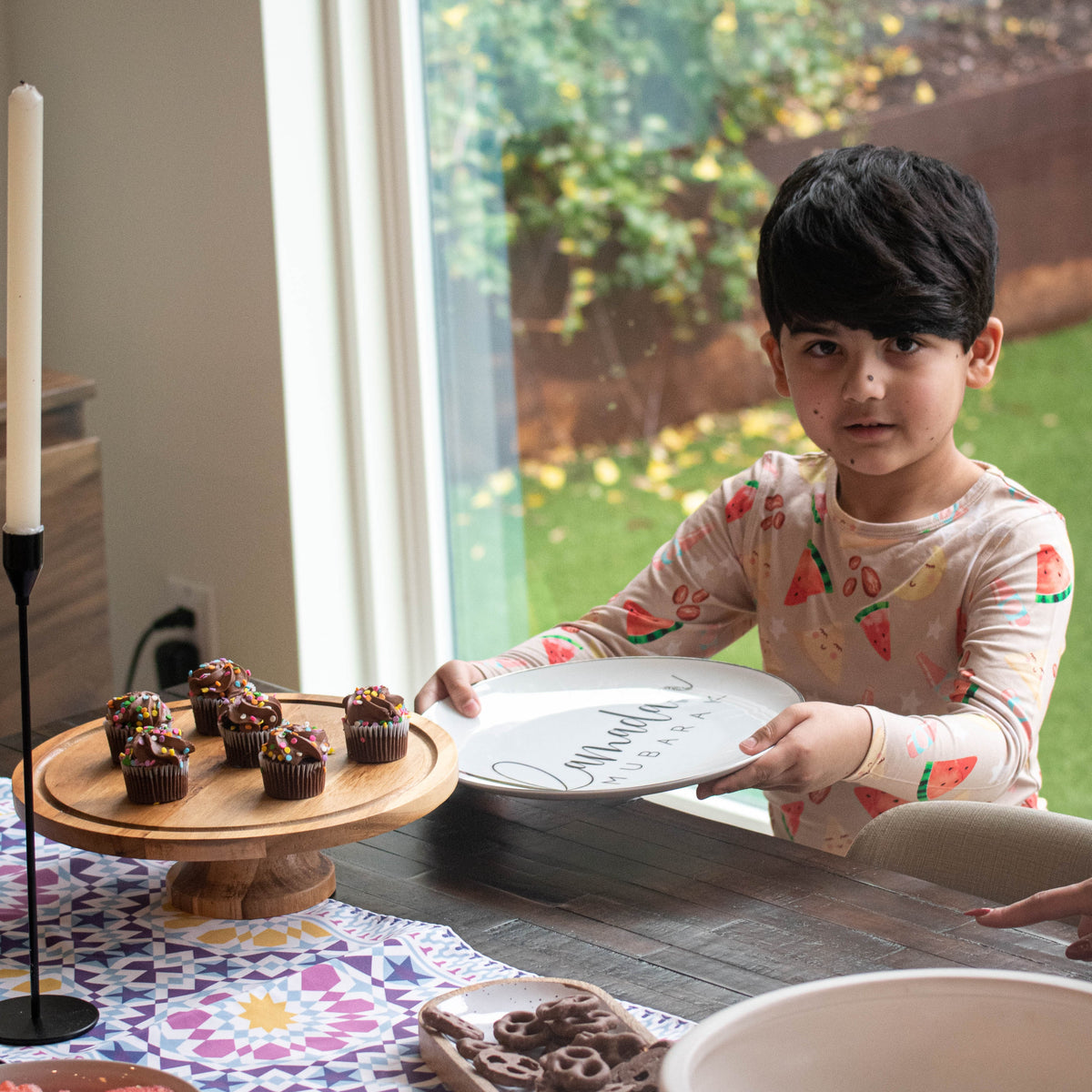 boy holding a a plate in front of a cupcake stand with chocolate cupcakes on it