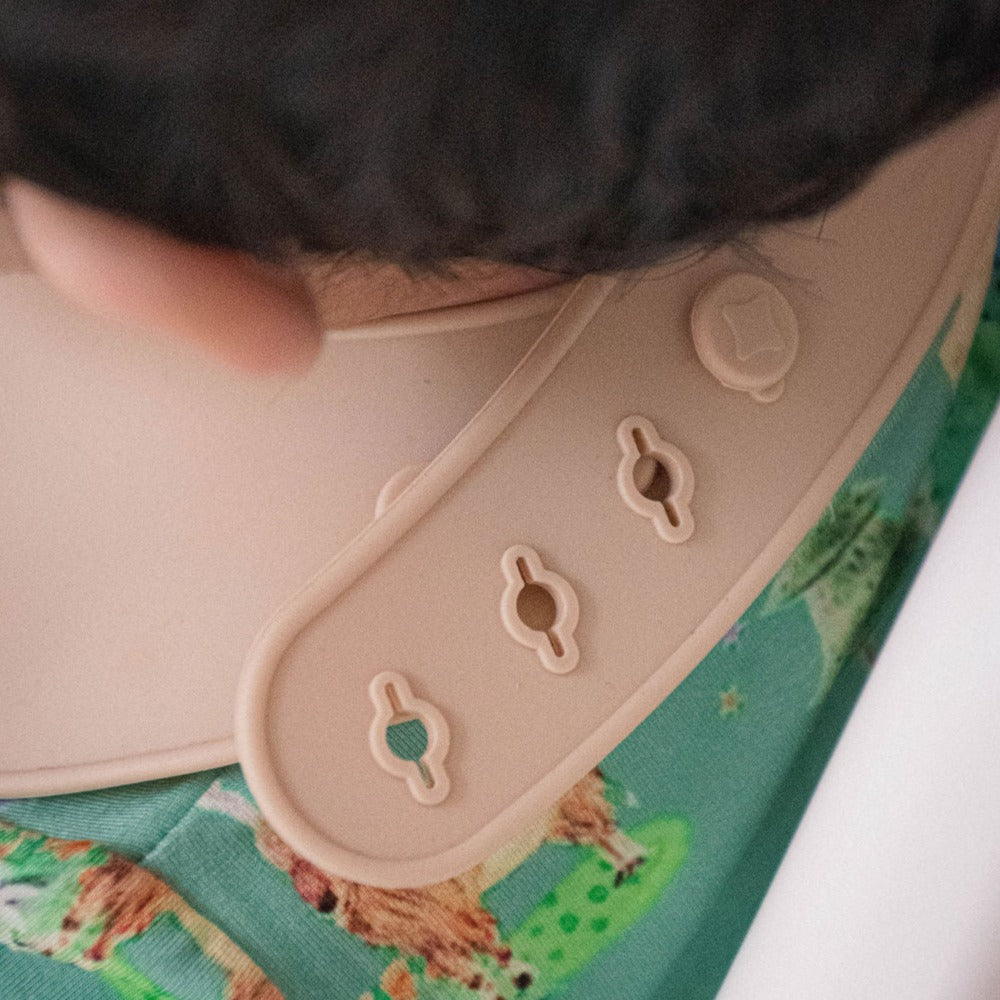 Close up of bib clasp closure with four reinforced holes.  Bib is closed in one hole.