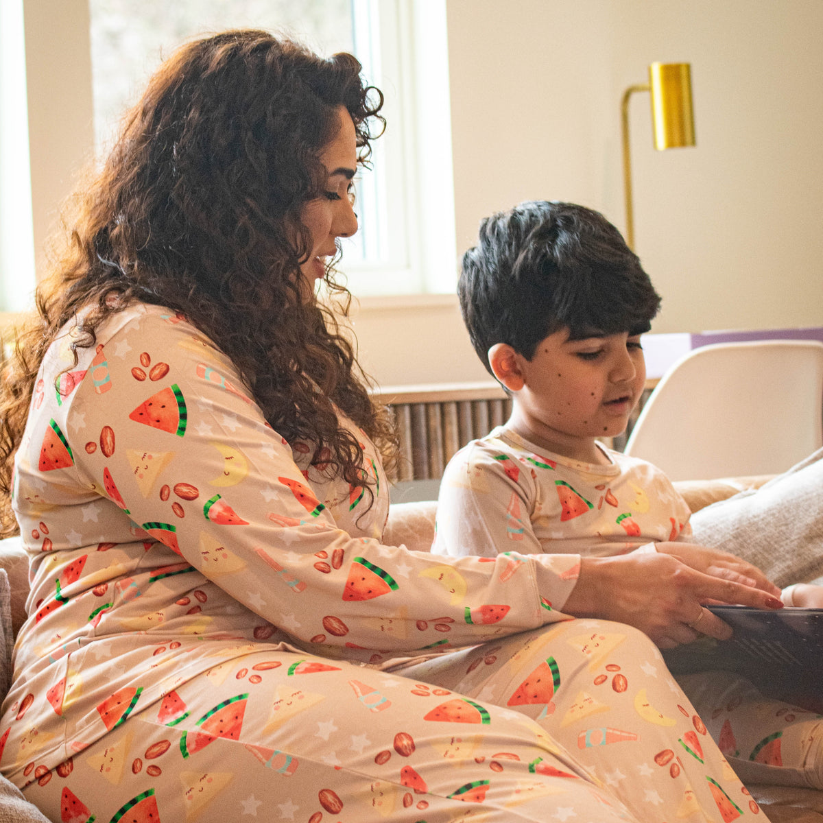 mother and son wearing matching pajamas on sofa.  pajamas have dates, watermelon, samosas and moons on them.
