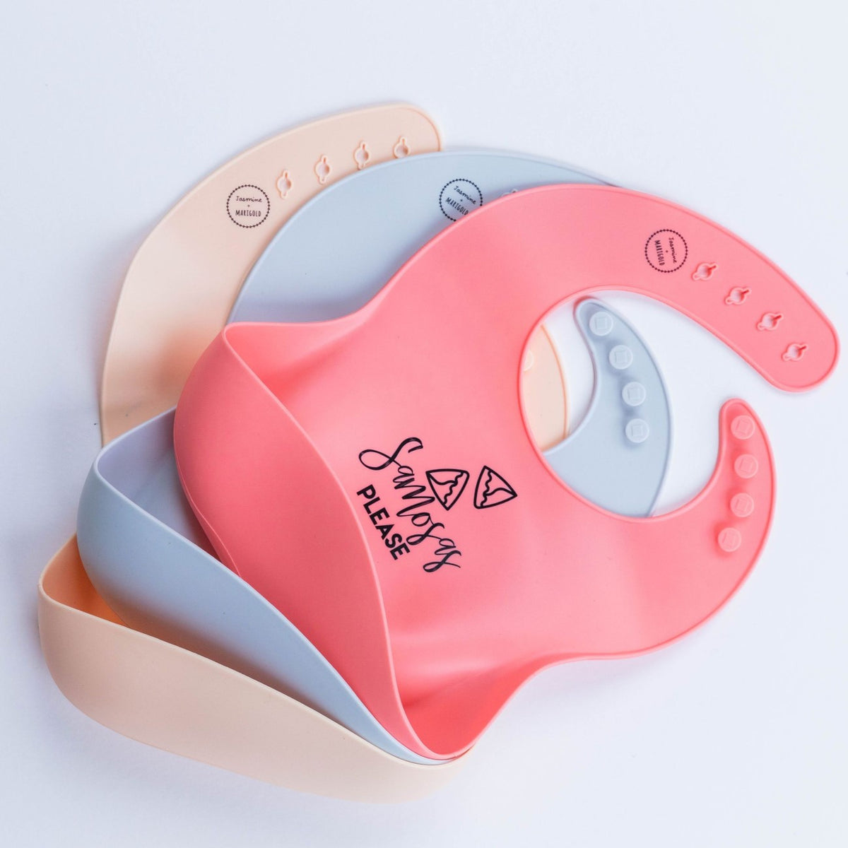 rosie, blue, and oat samosas please bibs laying on a white background.