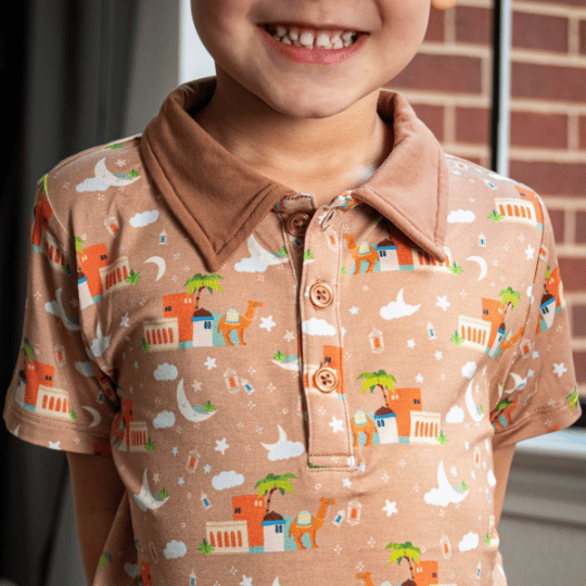 A child wearing a beige polo shirt with a printed design featuring desert scenes and cultural motifs.