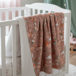 White crib with a pink blanket featuring animal prints in a nursery setting.