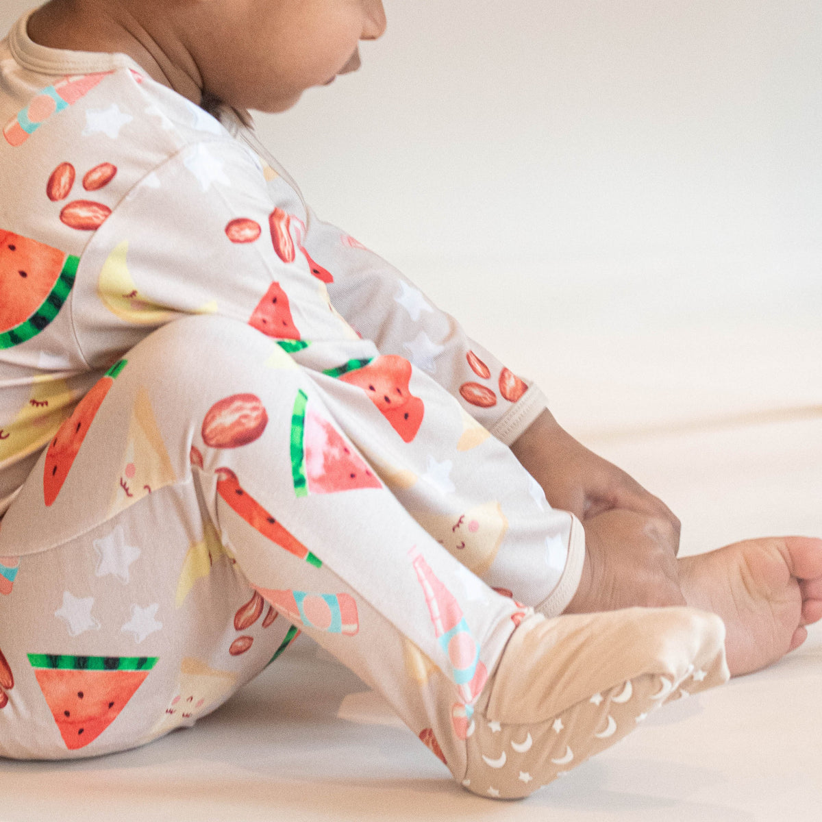 child sitting on ground wearing pajamas in moon star watermelon and date print