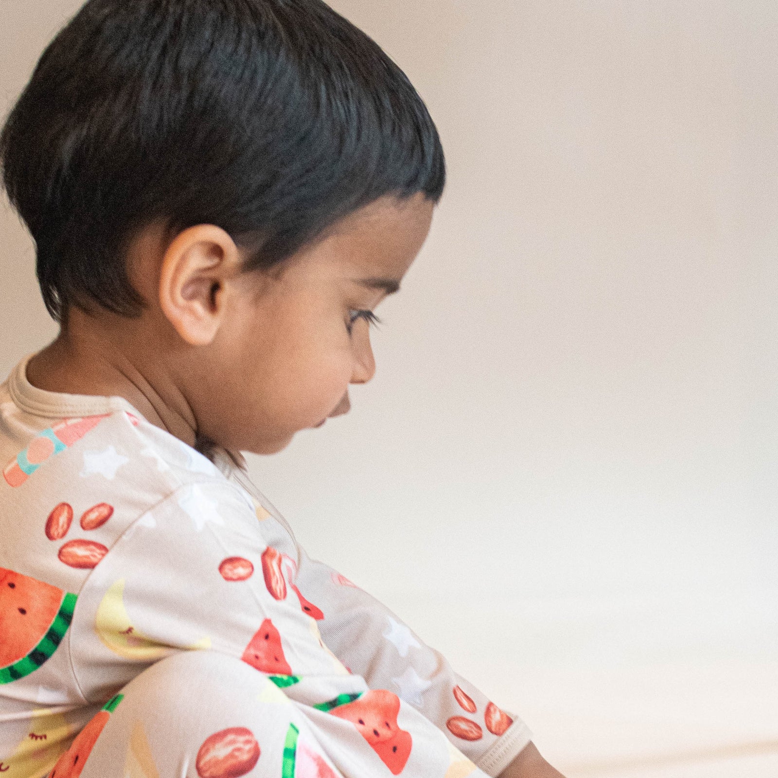 child sitting on ground wearing pajamas in moon star watermelon and date print