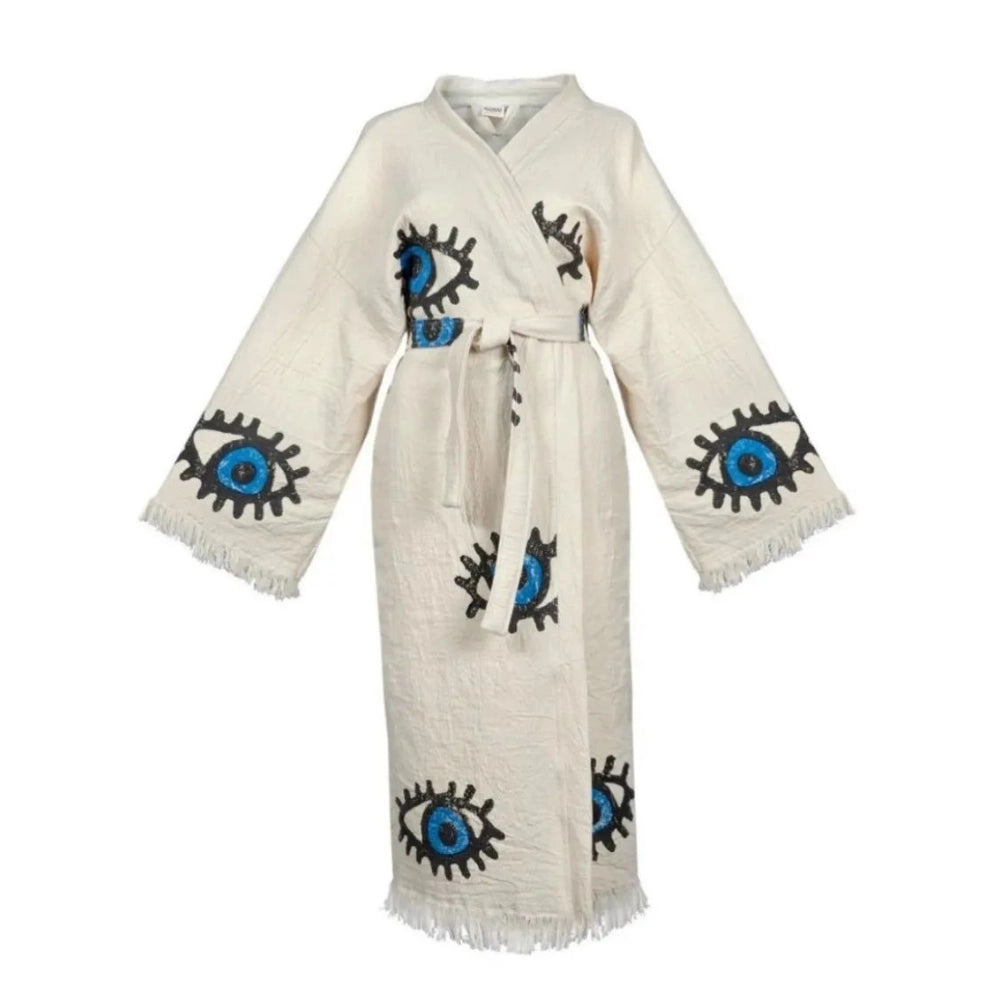 The image shows a white kaftan-style robe made from 100% organic Turkish cotton. The robe features a relaxed fit with wide sleeves and a belted waist. It is adorned with embroidered eye motifs in vibrant colors, adding an artistic and unique touch. The fabric has a textured, slightly crinkled appearance, enhancing its casual and comfortable feel. Made in Turkey, this robe combines traditional craftsmanship with modern design elements.