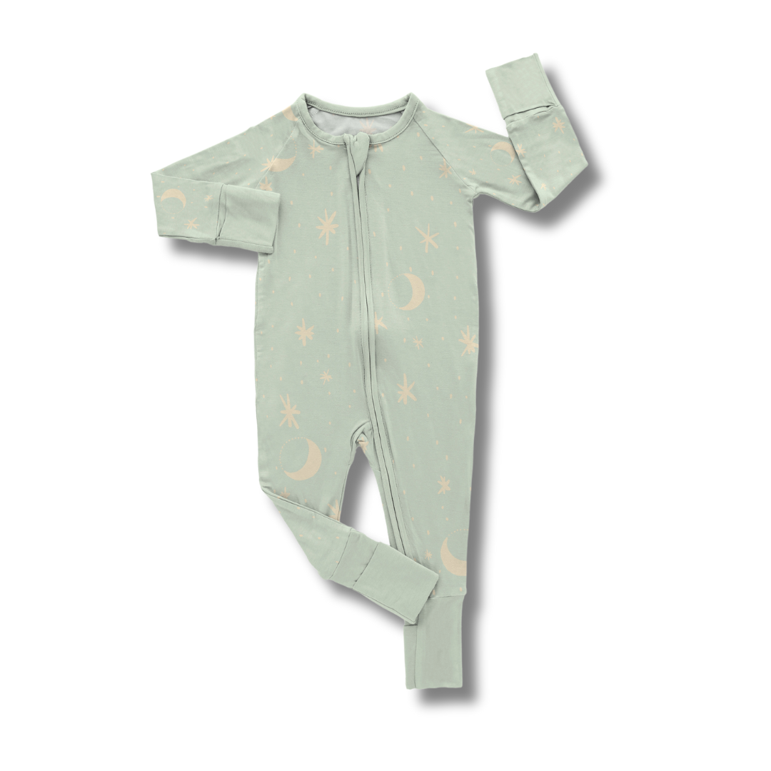A smiling baby wearing a sleep sack with a crescent moon and stars pattern on a mint background.